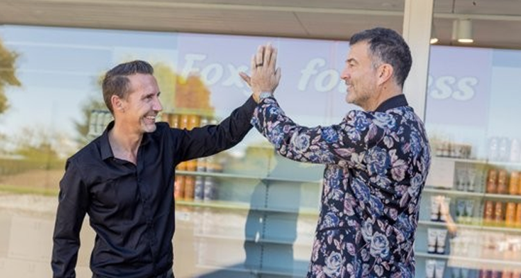 To smilende mænd foran en Hi Five-butik giver hinanden en high five – et stærkt billede til sektionen om os.